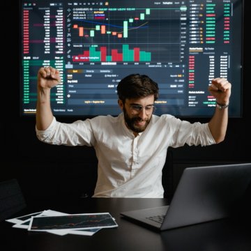 A man with his arms above his hands looking at a computer with stocks